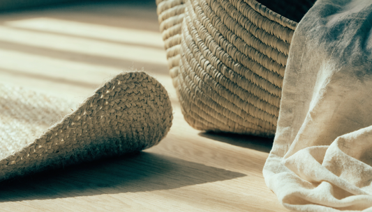 Close up of natural fibre textures on pale oak: the rolled corner of a jute rug, a folded seagrass basket and a soft cotton cloth